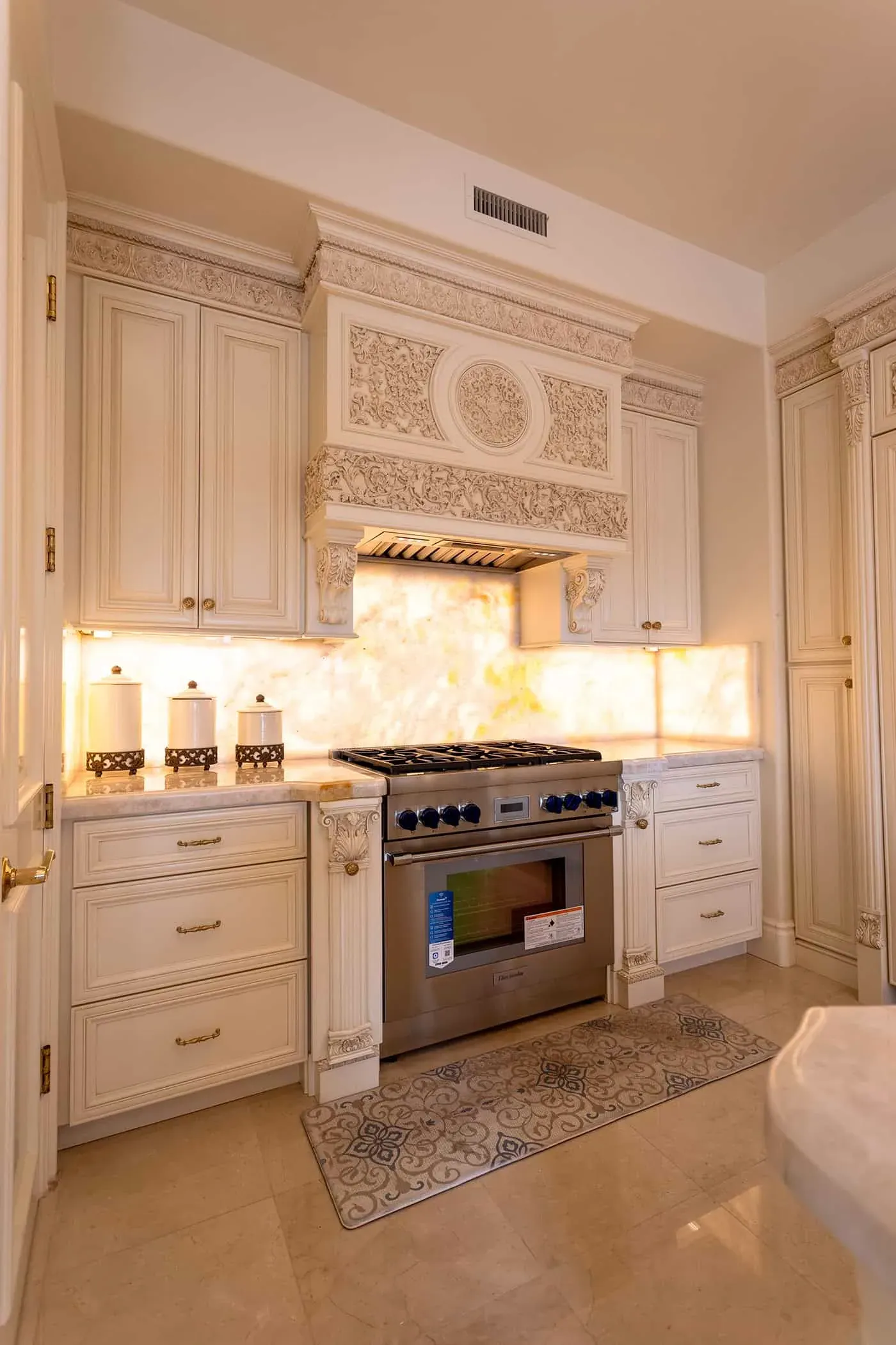 Backlit onyx backsplash behind a stainless range in carved cream cabinetry