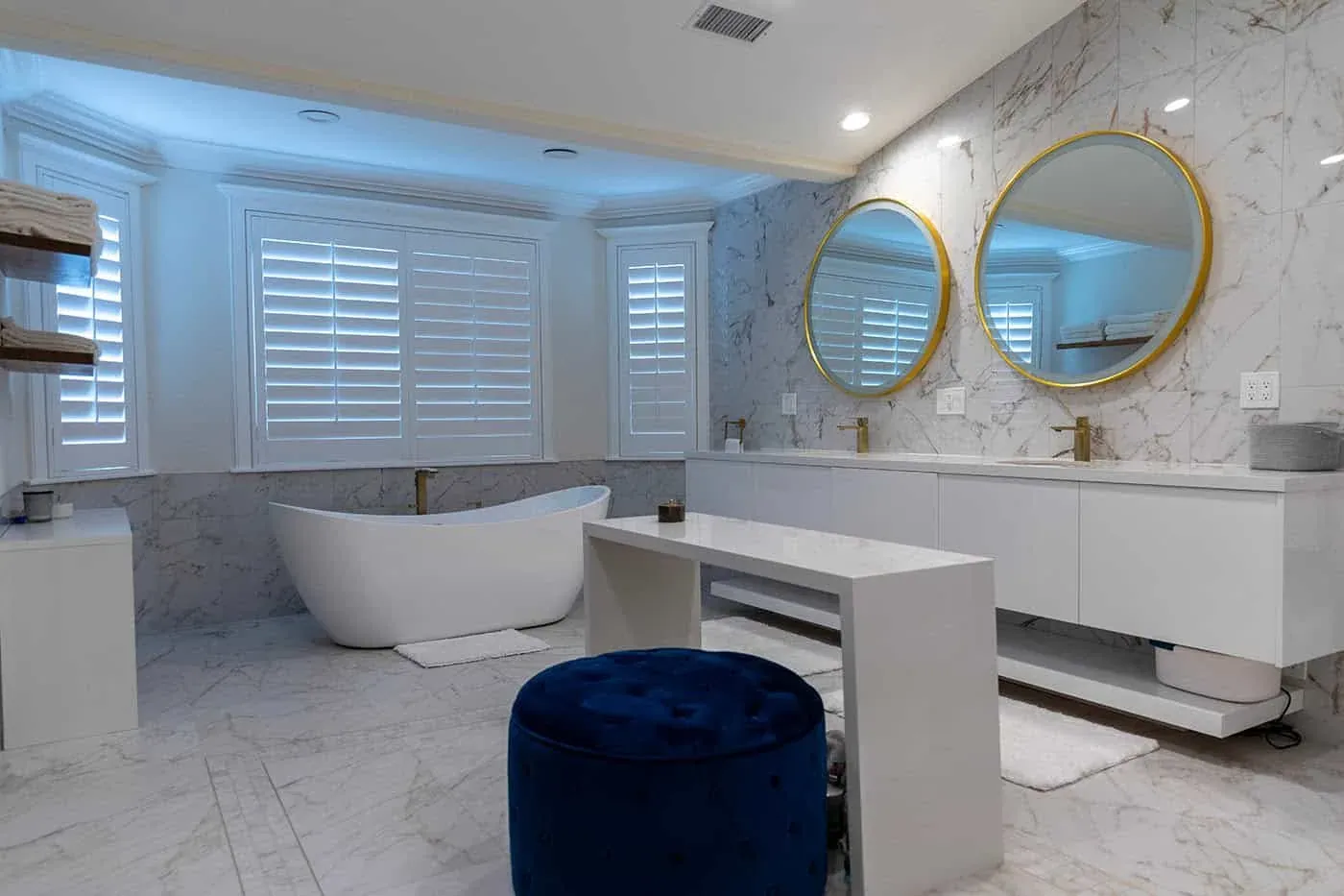 Bathroom with round gold mirrors, shutters and a freestanding tub