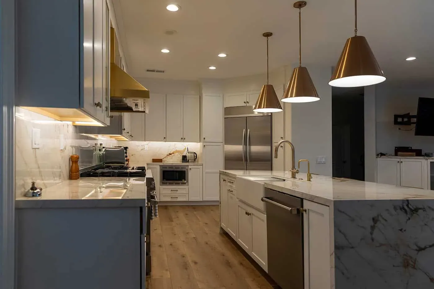 Brass hood above a stainless range with a marble backsplash and pendant lighting