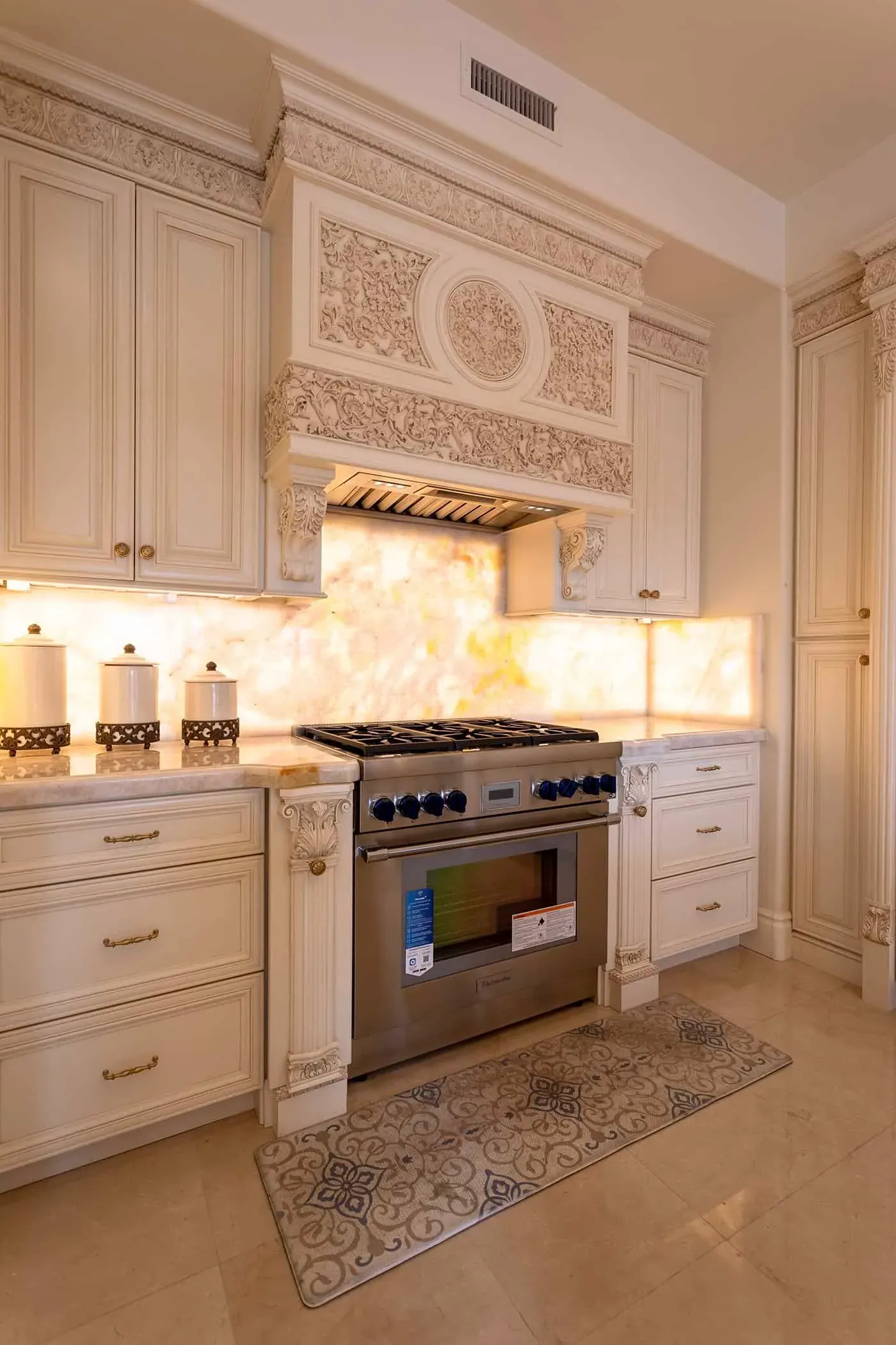 Carved cabinetry with a backlit onyx backsplash and professional range