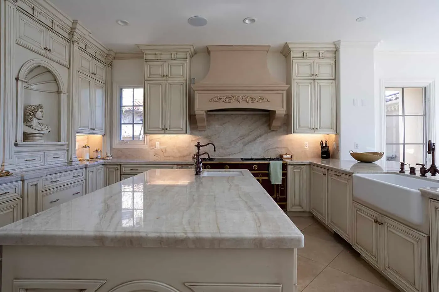 Carved cream cabinetry with an arched hood surround beside a marble island