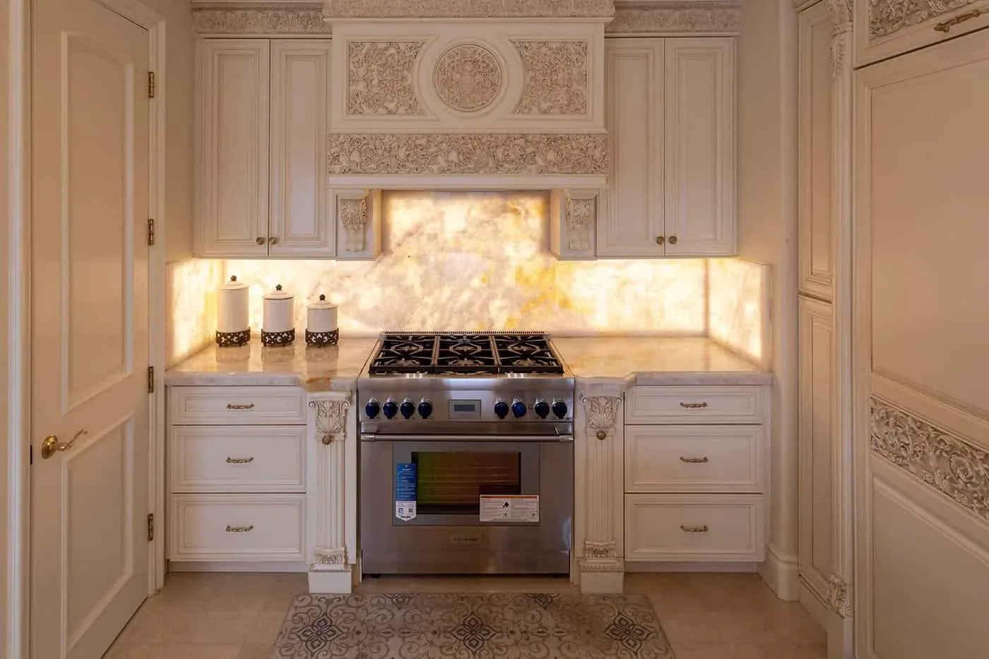 Carved cream cabinetry with a range and backlit onyx panels