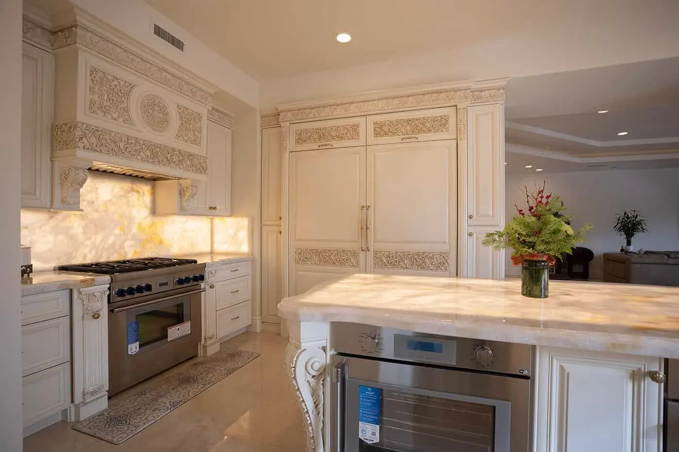 Carved cream cabinetry with a stainless range and a backlit onyx backsplash