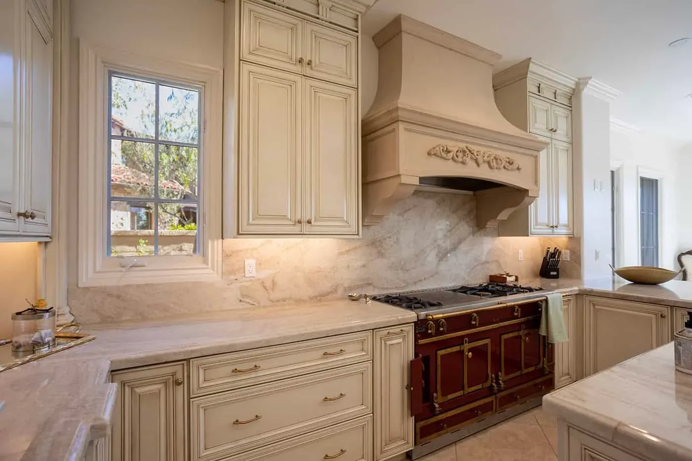Carved hood above a red range beside a window and stone counters