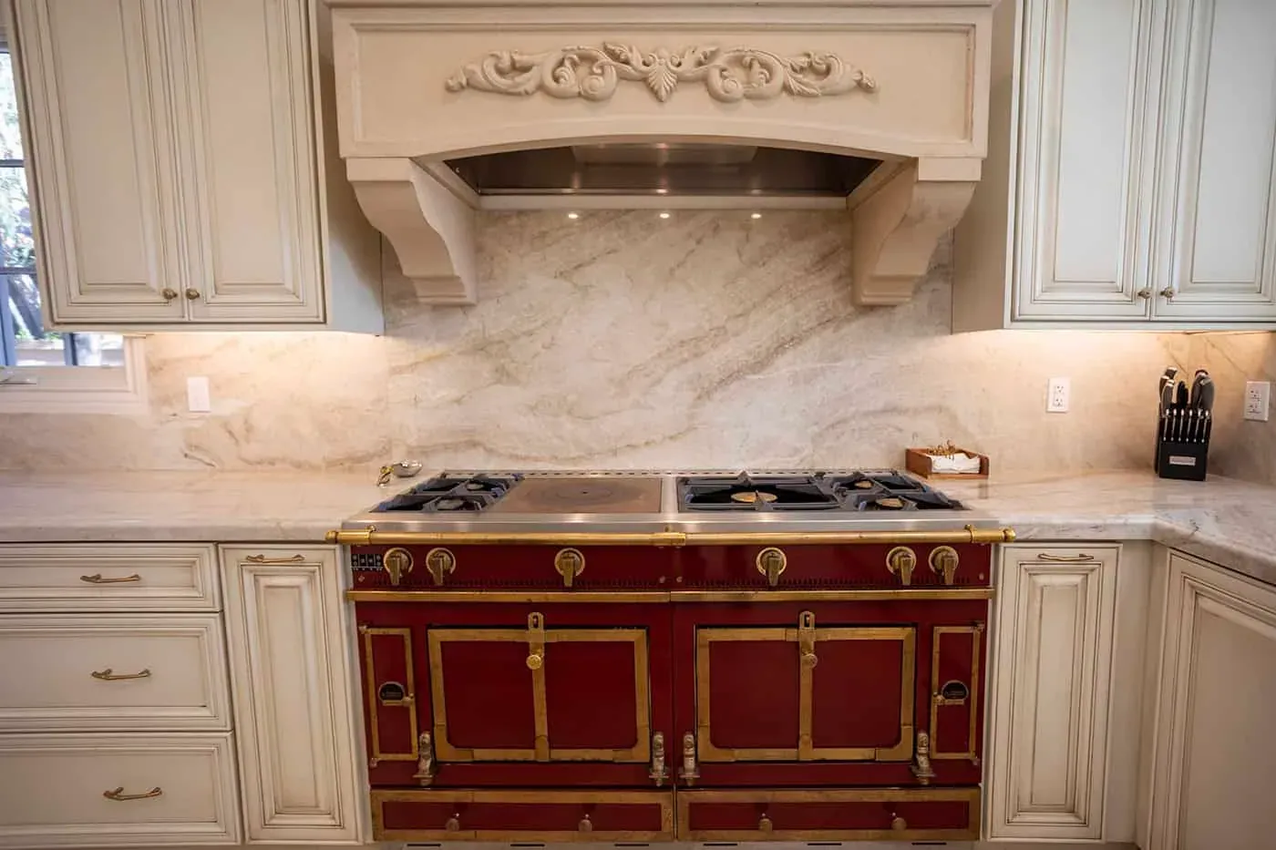 Carved hood over a red range with a stone slab backsplash