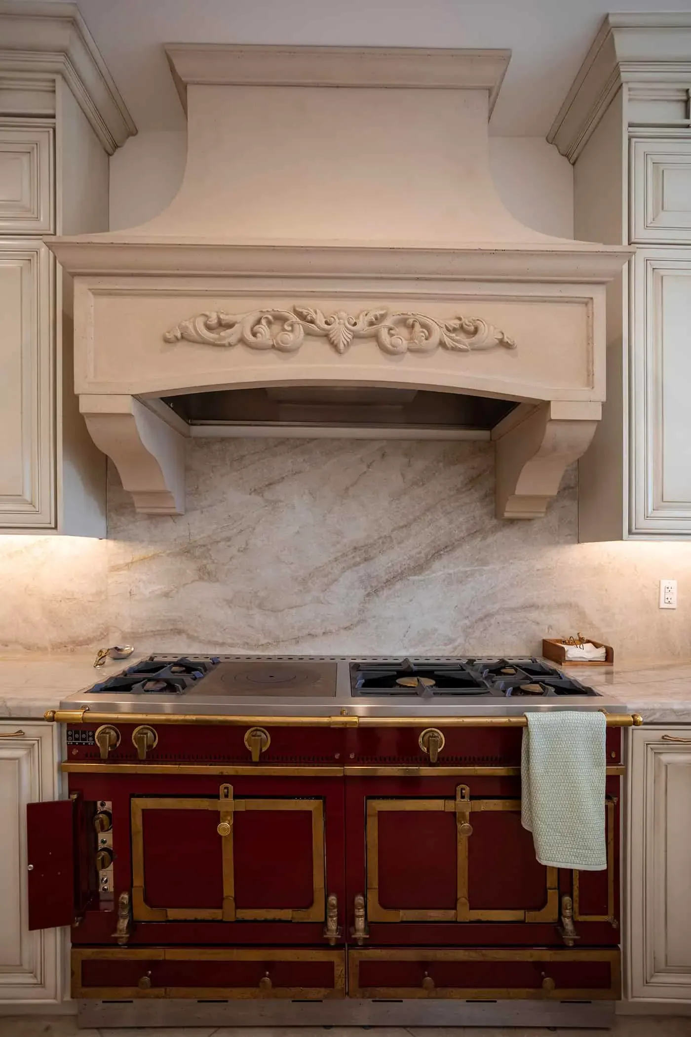 Carved hood surround above a red professional range with a stone backsplash