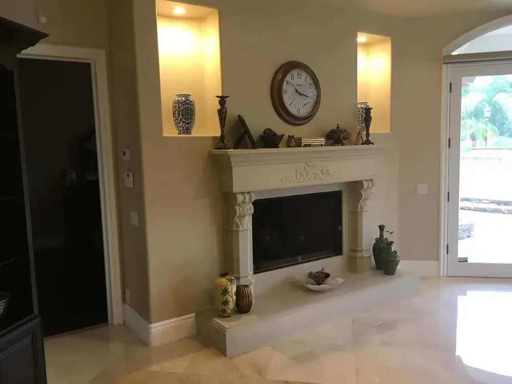 Polished large-format travertine floor tiles laid through a living room with a carved stone fireplace