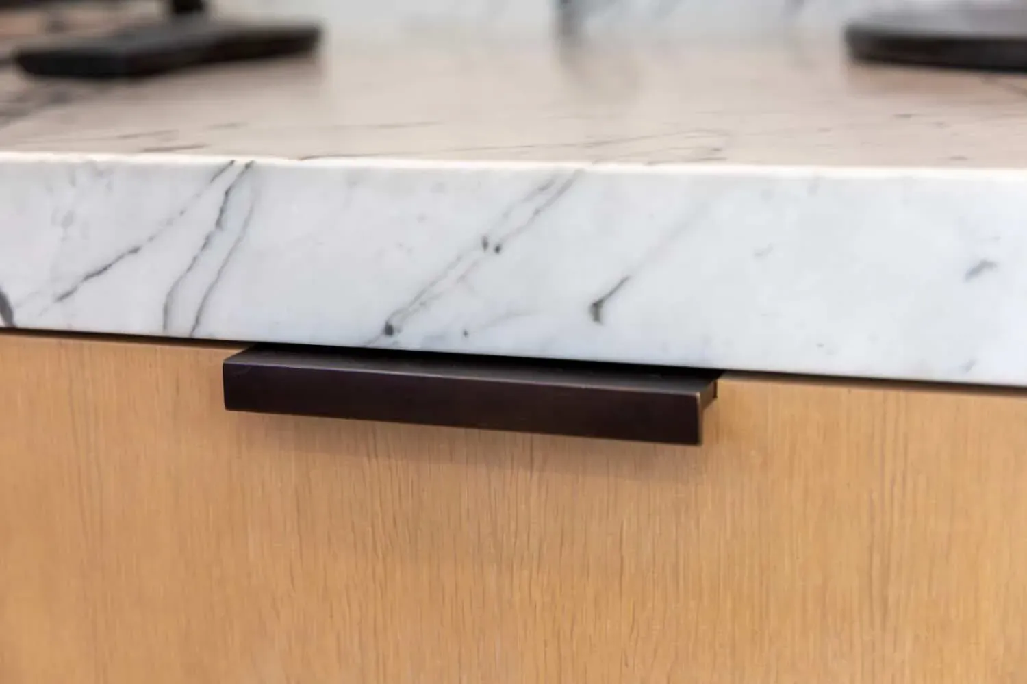 Close view of a marble worktop edge and a black cabinet pull