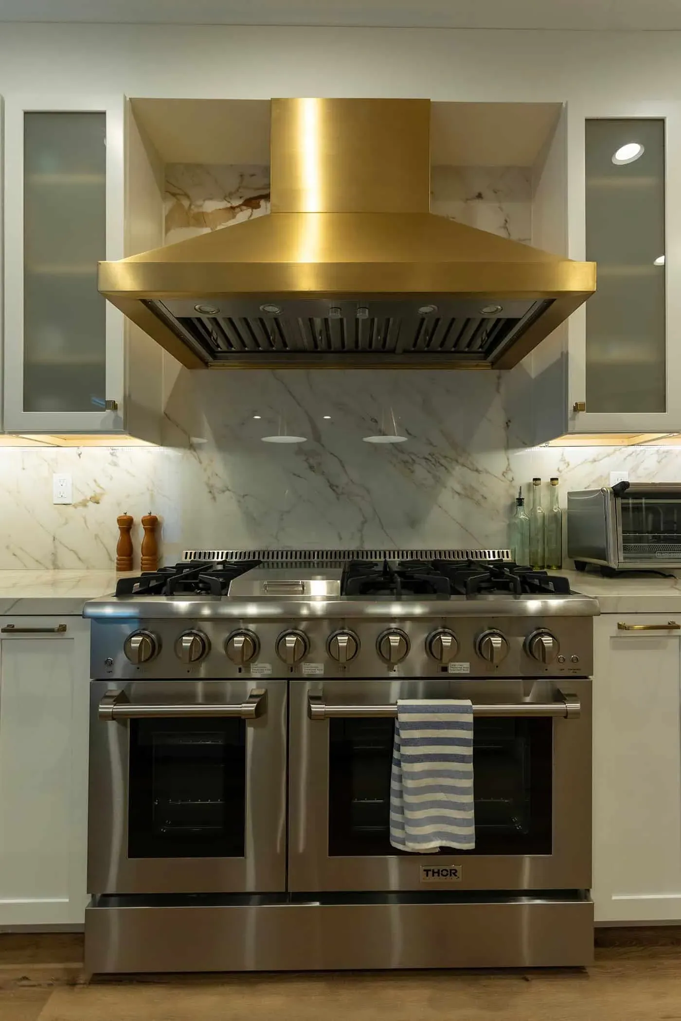 Close view of a professional range and brass hood against a marble backsplash
