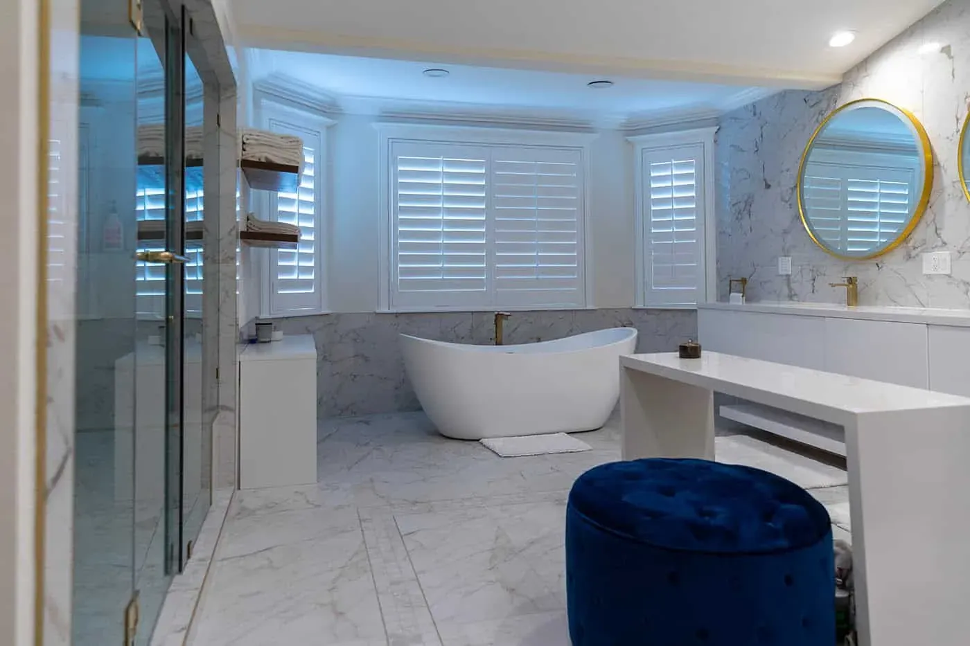 Corner of a marble bathroom with a glass shower and gold-framed mirror