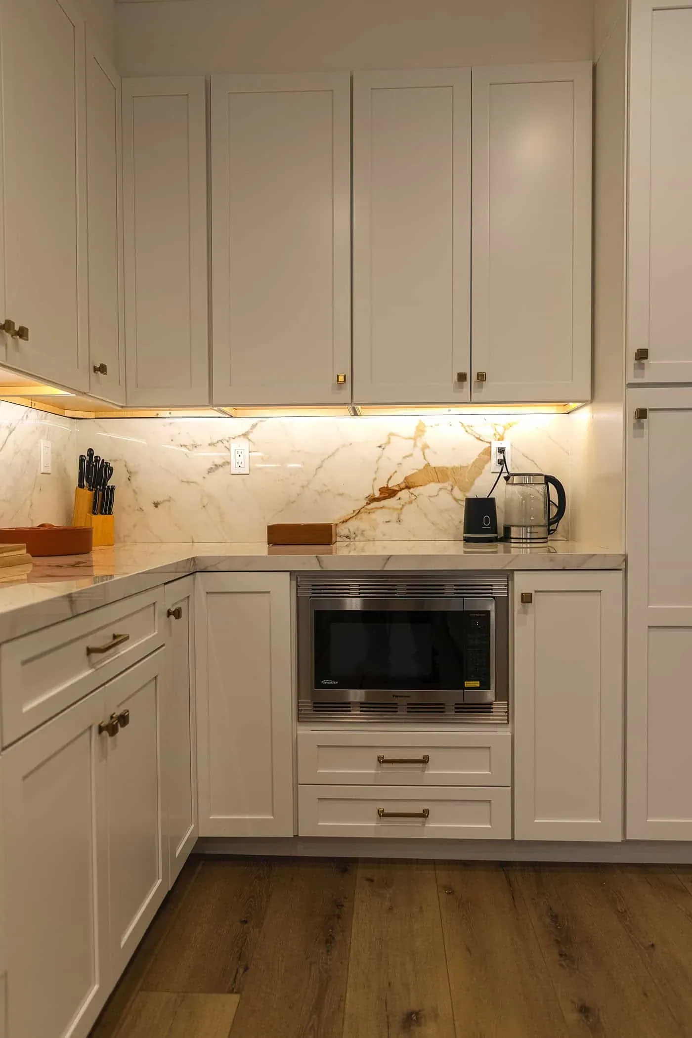 Cream cabinetry with a built-in microwave, marble backsplash and under-cabinet lighting