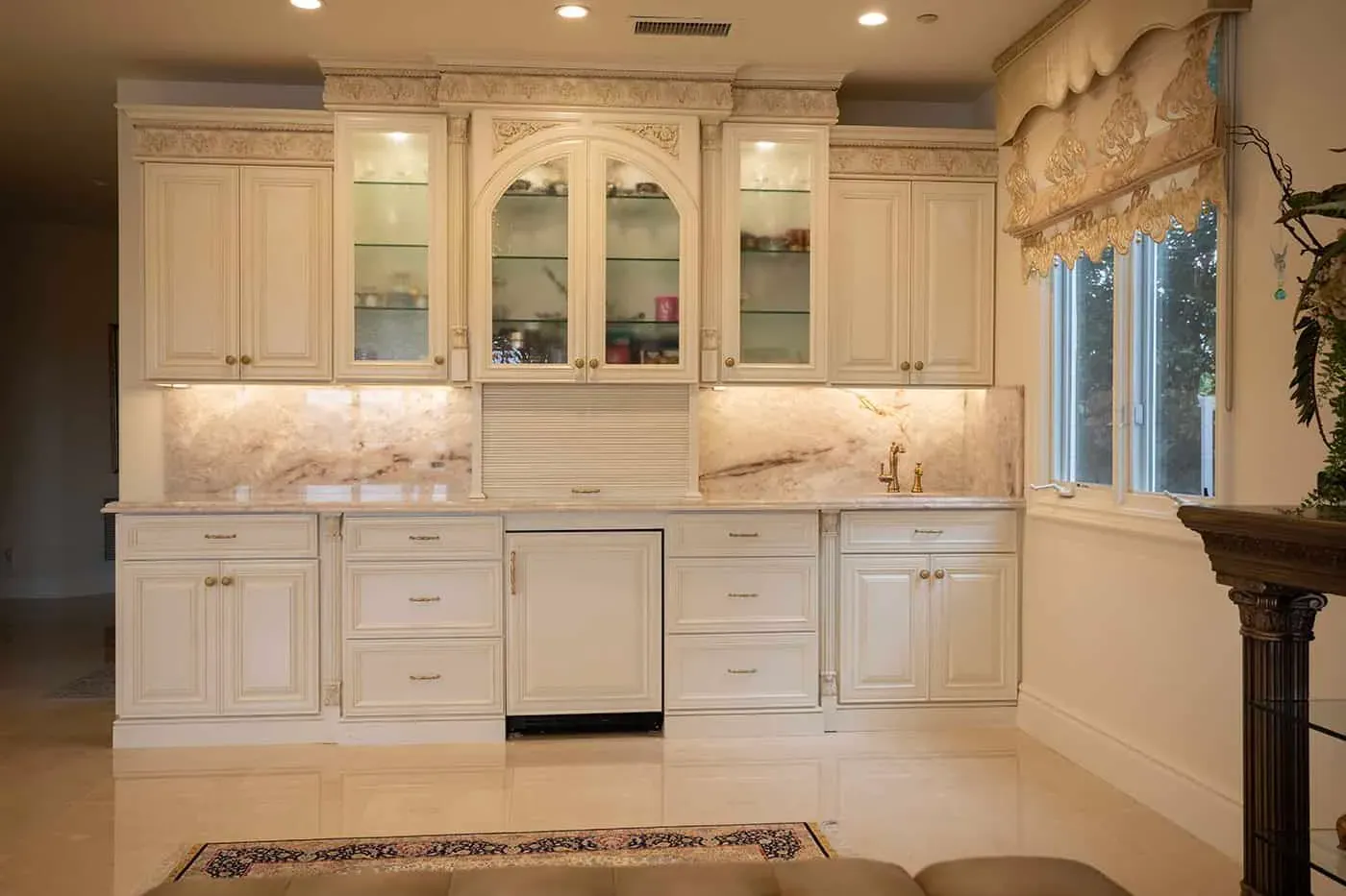 Cream cabinetry with glass doors, a panelled dishwasher and onyx backsplash