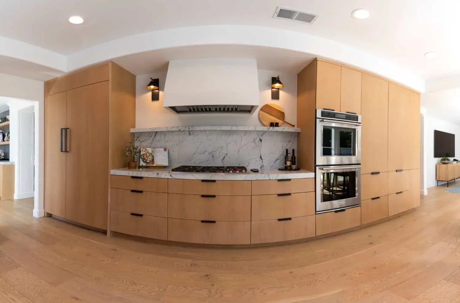 Curved plaster hood above a cooktop with marble backsplash and wall ovens