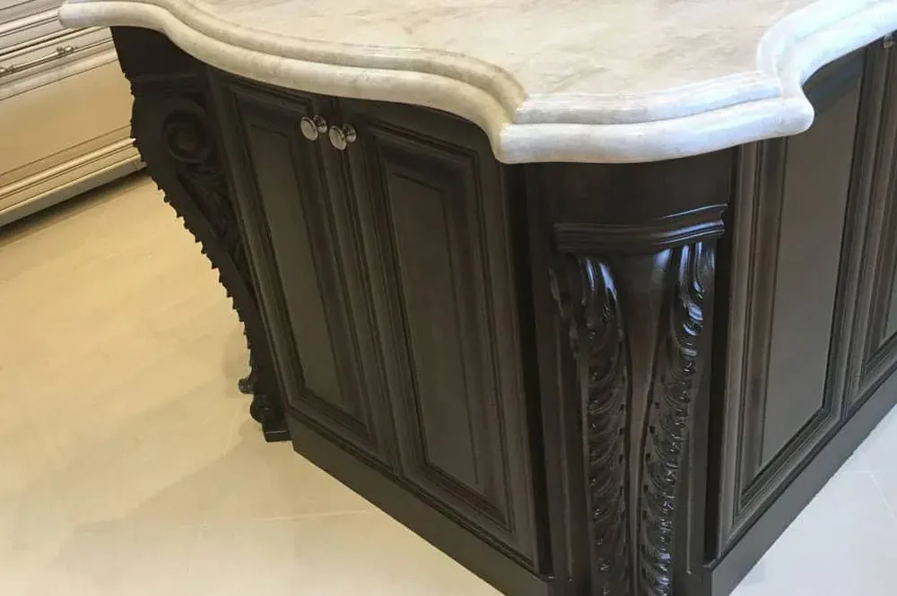 Carved corbel detail on an espresso stained cabinet end panel under a light stone countertop with an ogee edge