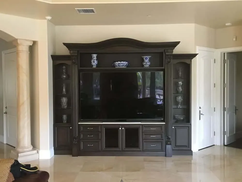 Dark built-in media wall with arched crown moulding and glass display cabinets