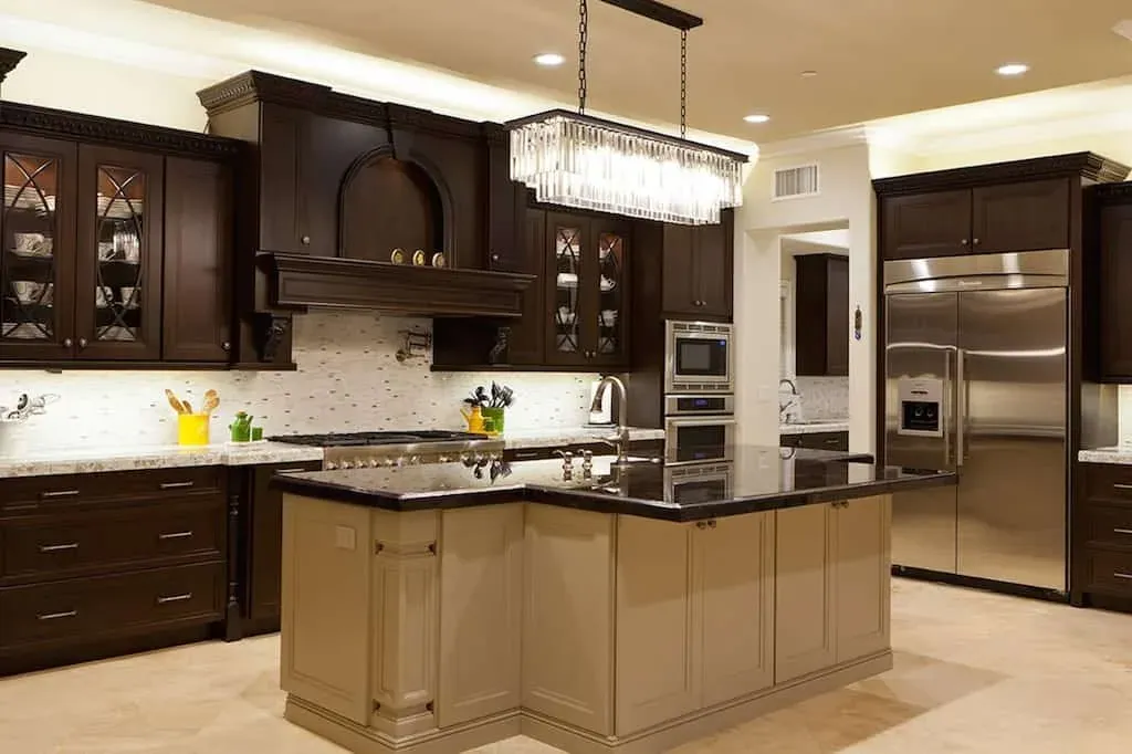 Dark kitchen with a linear chandelier, granite island and wall ovens