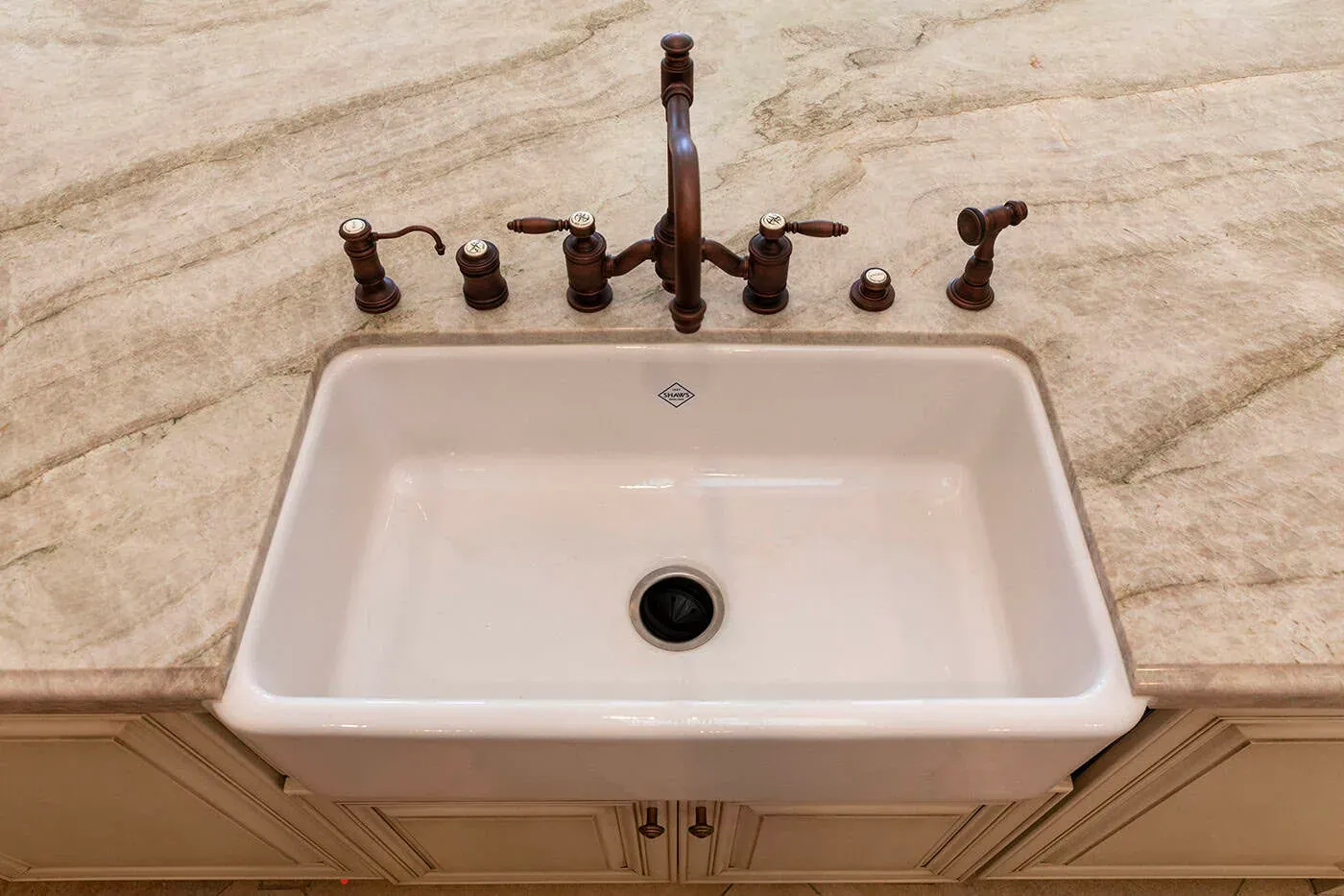 Farmhouse sink with a bronze bridge tap on a veined stone counter