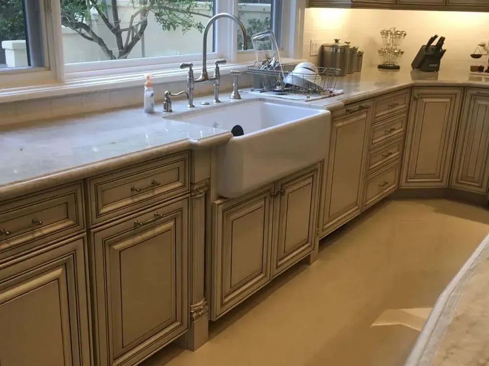 Travertine flooring beside a farmhouse sink run in a glazed traditional kitchen