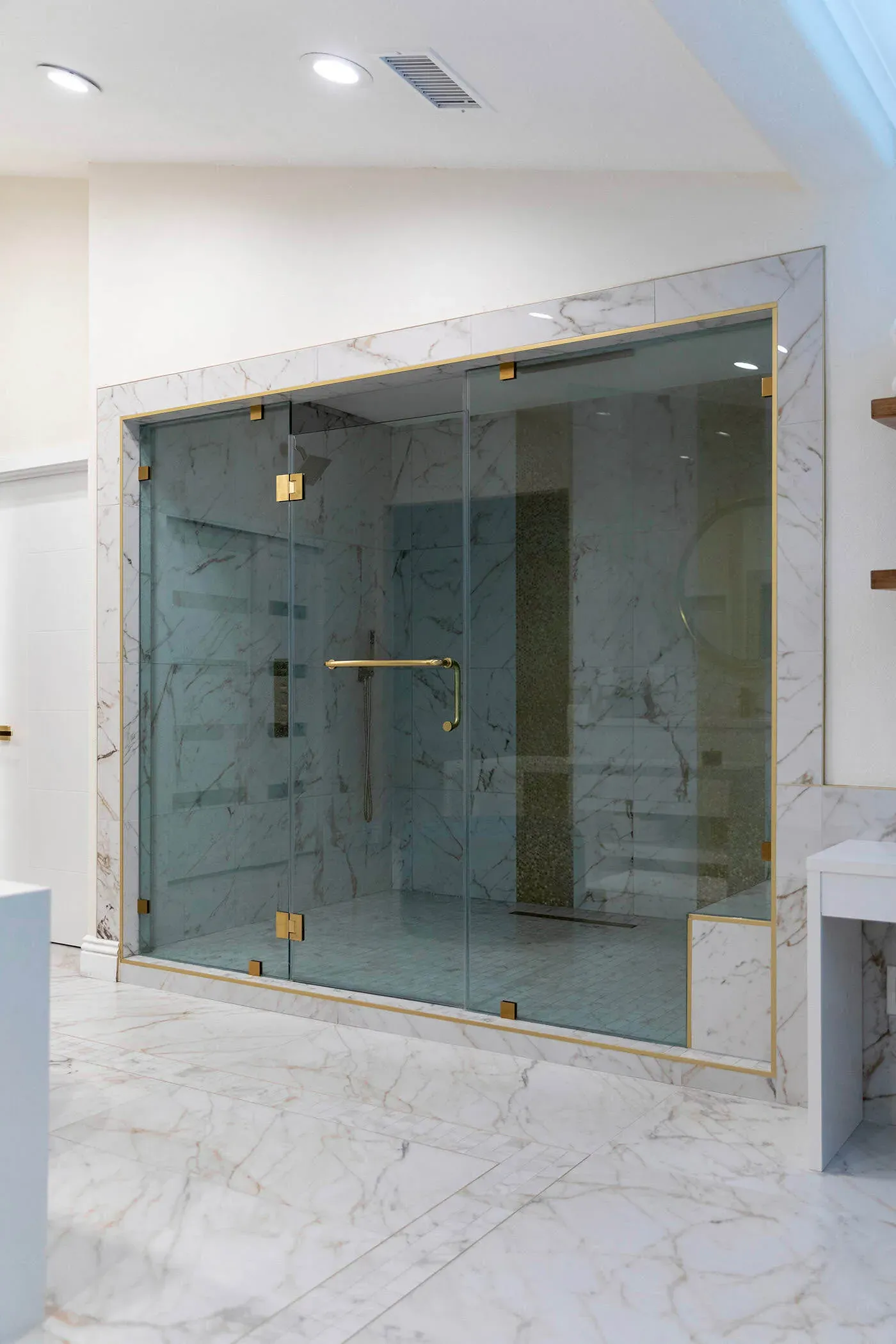 Frameless glass steam shower enclosure with marble walls and brass fittings