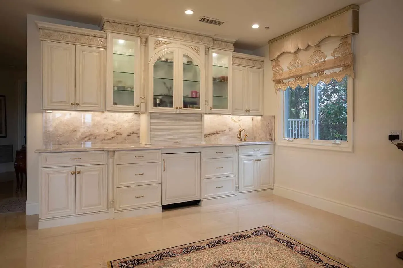 Glass-front cream cabinetry beside a window and a patterned rug