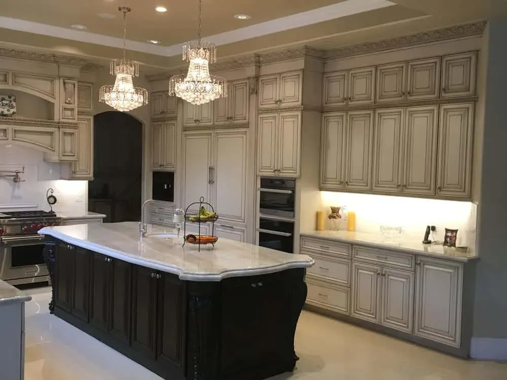 Glazed cabinetry with two chandeliers above a dark island