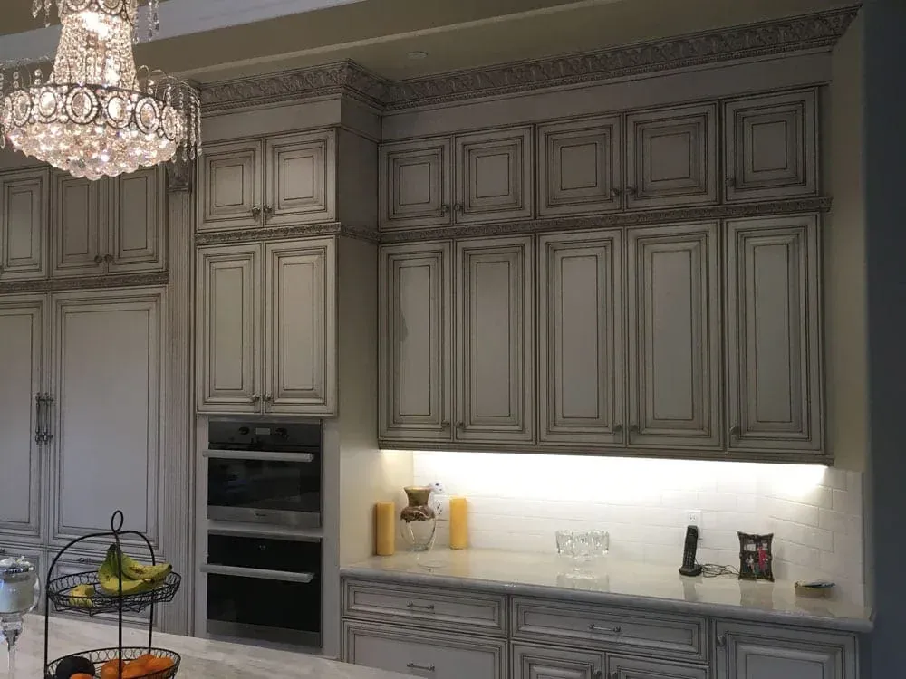 Glazed cabinetry wall with open display shelving beneath a crystal chandelier