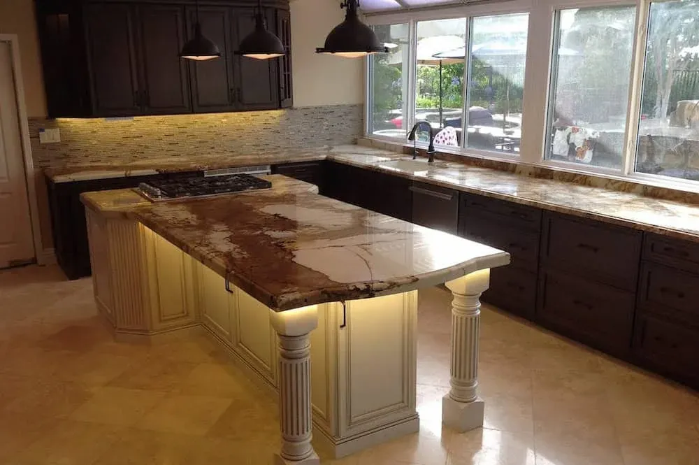 Figured granite island countertop on turned wood legs in a kitchen with dark perimeter cabinetry and pendant lights
