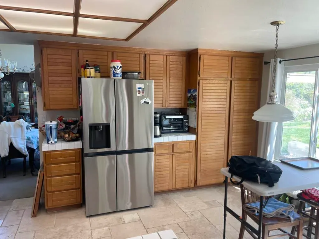 Honey oak kitchen before remodeling, with a fluorescent ceiling light box and tile floor