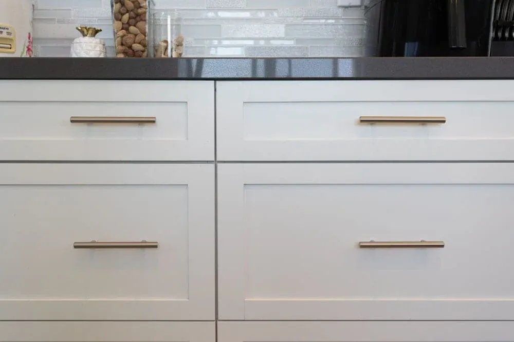 White shaker drawers with brass bar pulls beneath a dark worktop