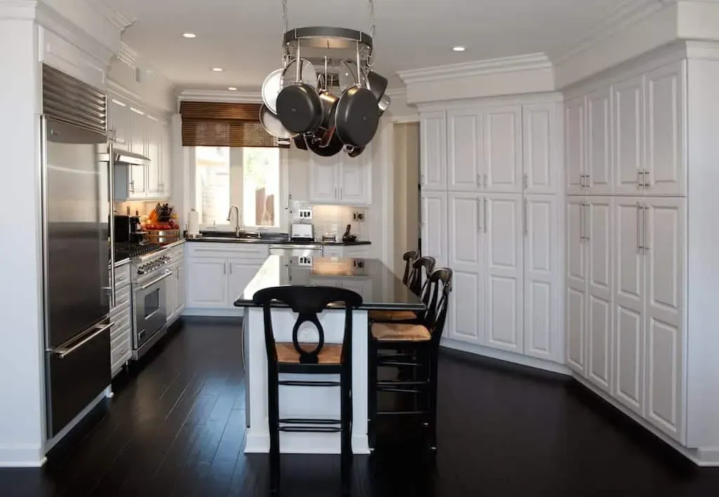 White kitchen with a hanging pot rack, dark island and dark wood floor