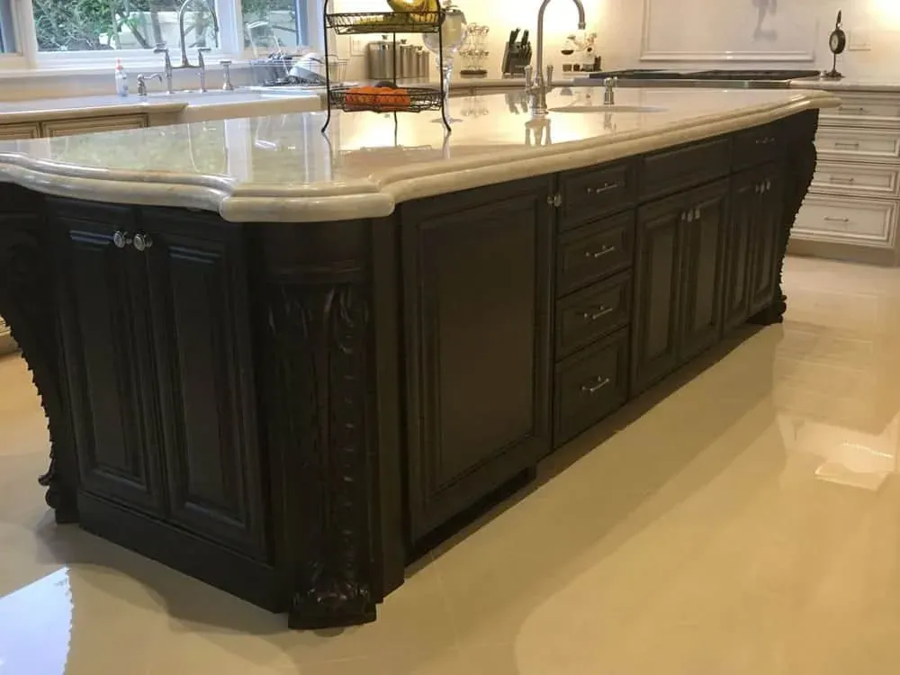 Dark carved island with a thick cream stone top and an ogee edge