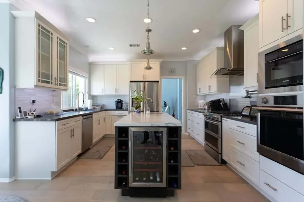 White kitchen with a dark island, wine cooler and stainless range