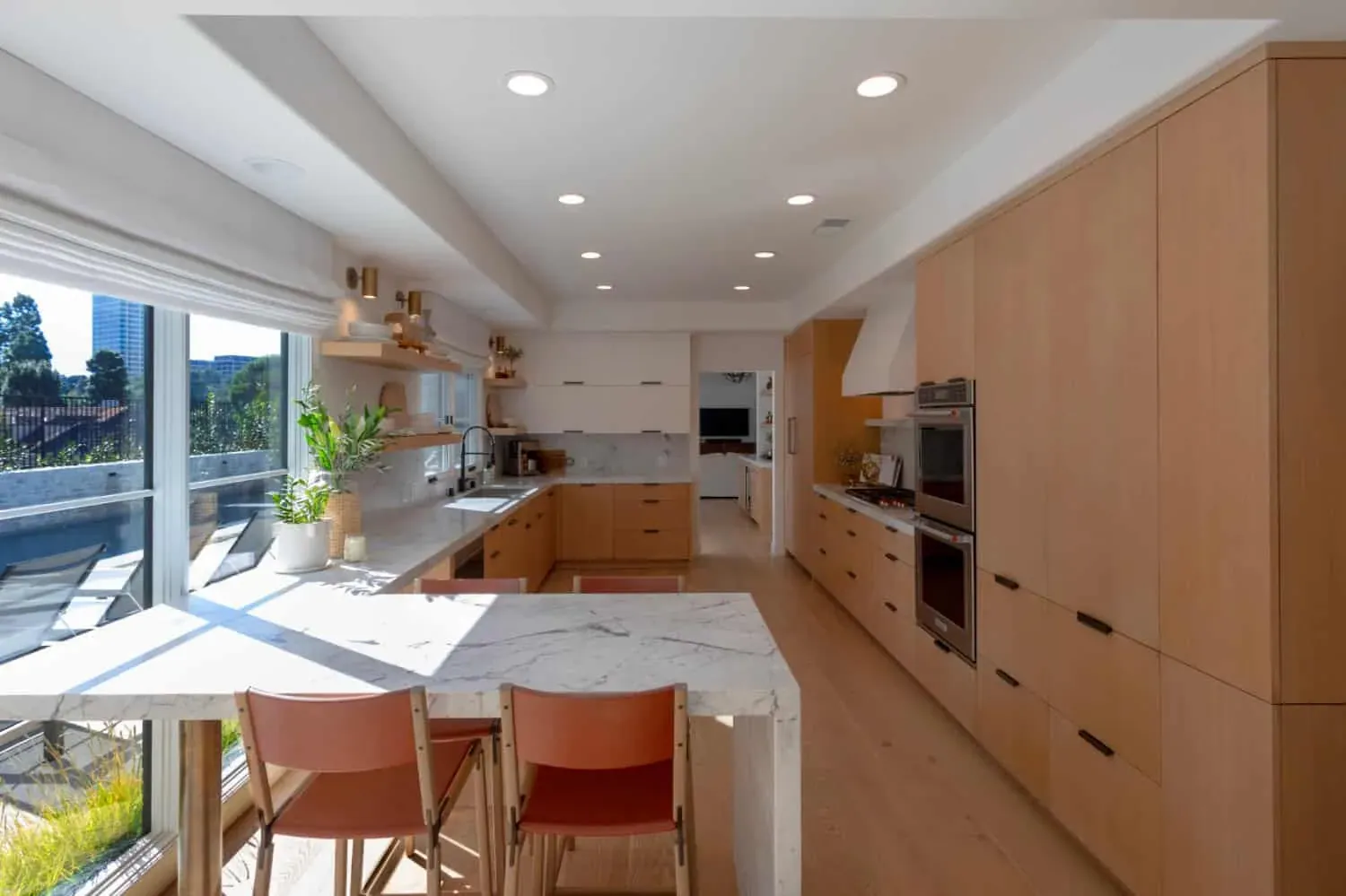 Light oak kitchen with a marble waterfall island and terracotta bar stools