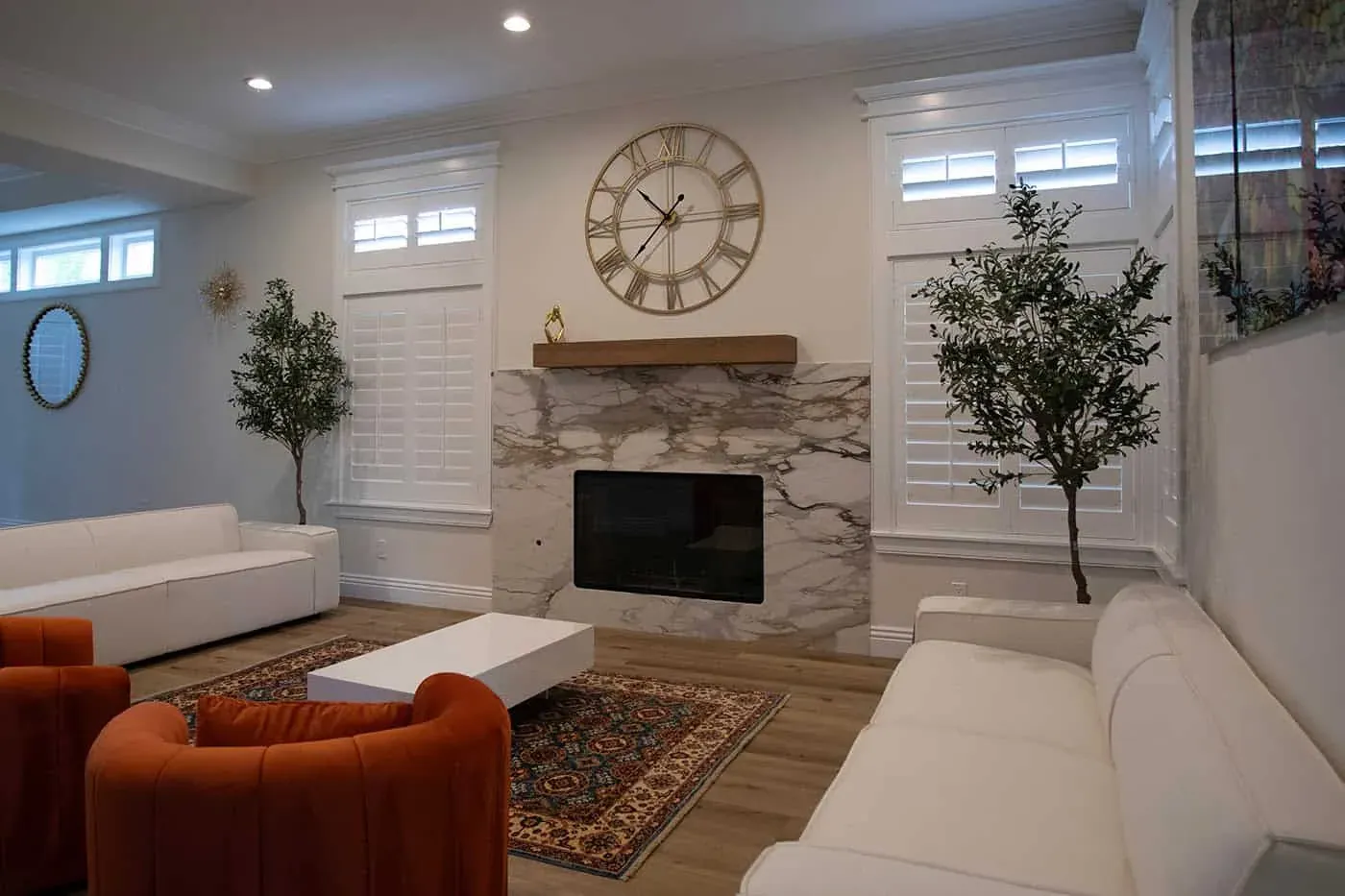 Living room with a marble fireplace, wall clock and orange armchairs