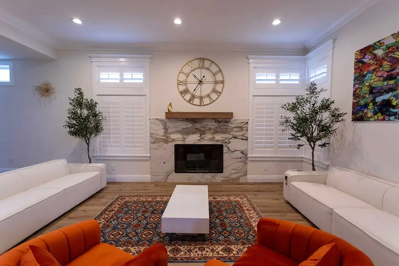 Living room with a stone fireplace, wall clock, olive trees and an orange sofa
