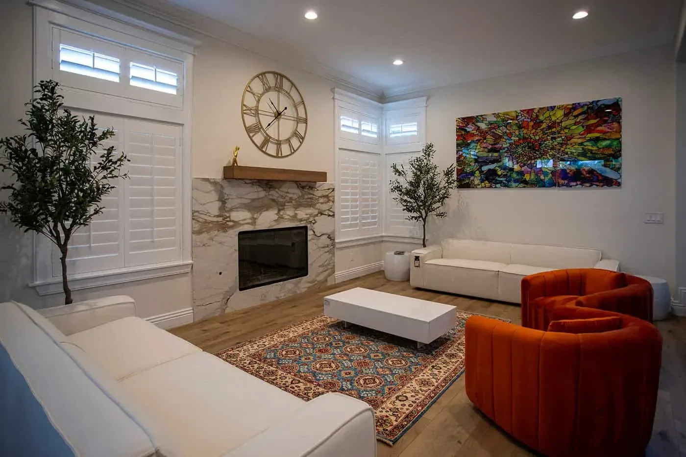 Living room with white sofas, an orange armchair and artwork above the fireplace