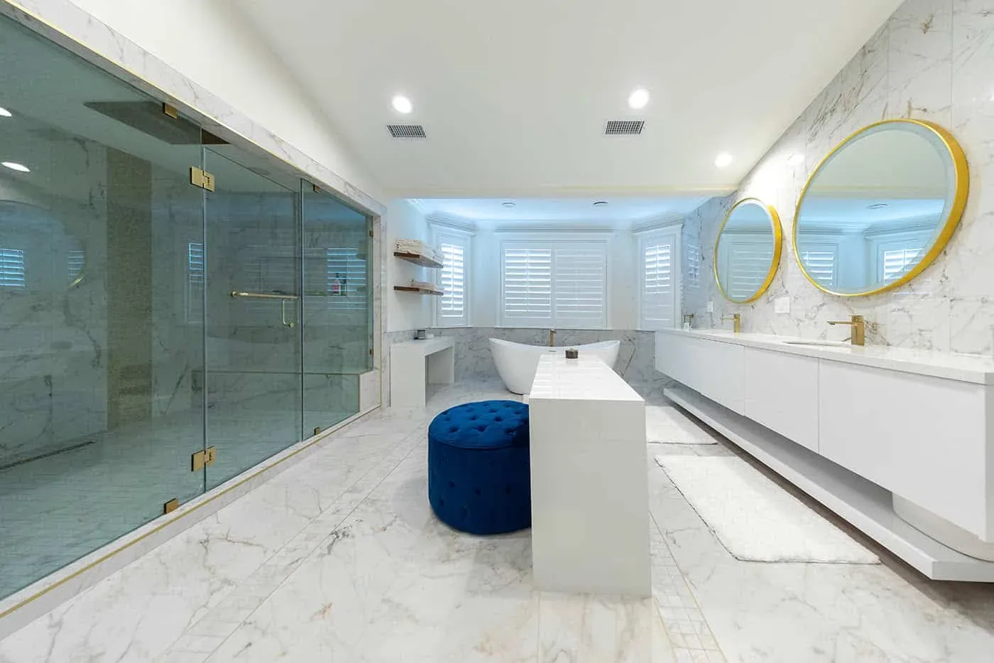 Marble bathroom with a glass shower enclosure, round gold mirrors and a freestanding vanity