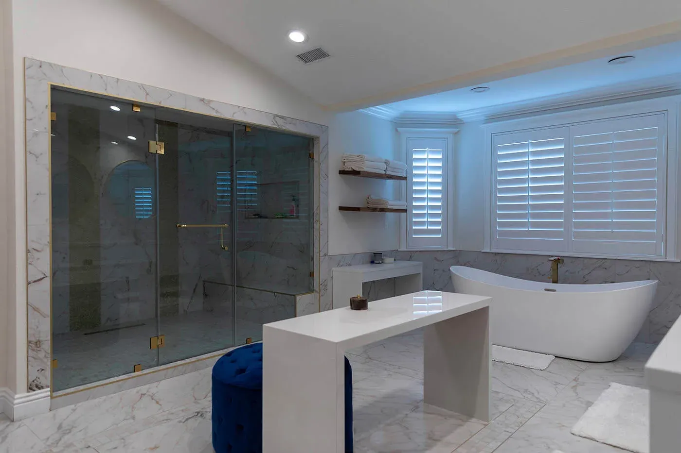 Marble bathroom with a glass shower, floating bench and freestanding tub