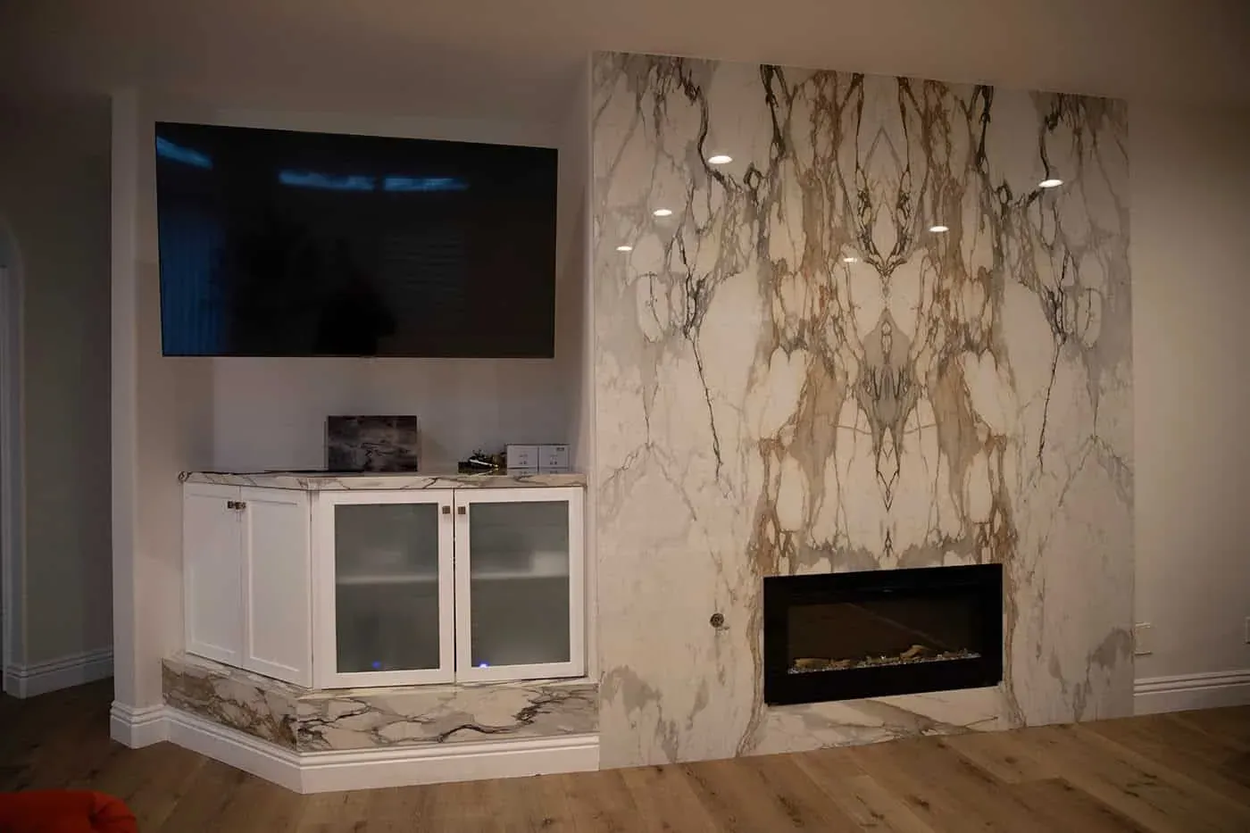 Marble fireplace wall with a television above white glass-front base cabinets