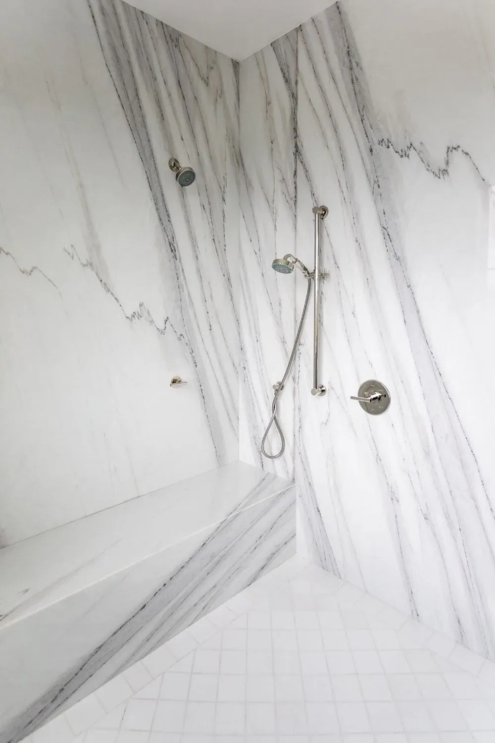 Marble shower wall with a handheld shower and chrome valve