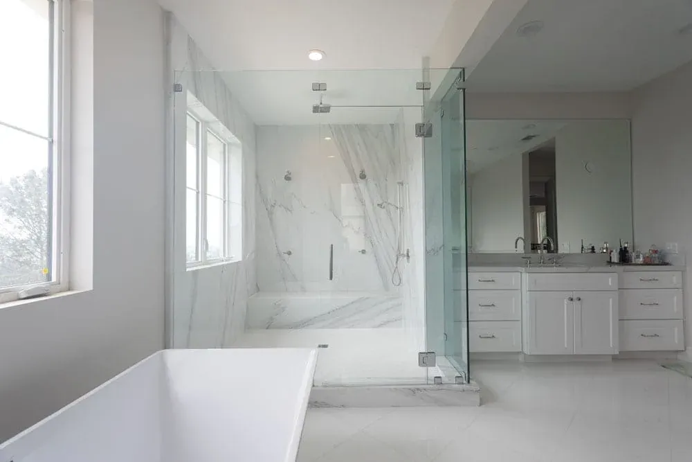 Marble slab shower with frameless glass beside a freestanding tub