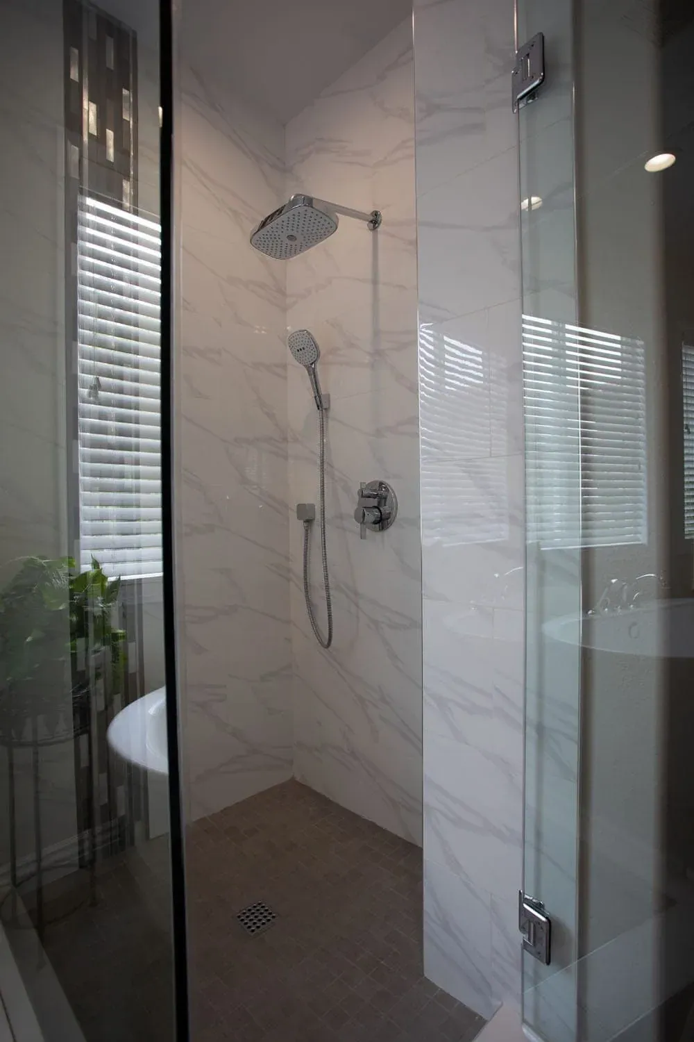 Marble-tiled shower with a handheld shower and a glass screen