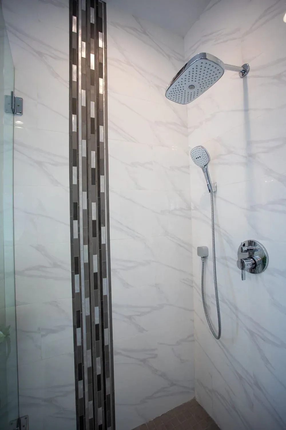 Marble-tiled shower with a mosaic accent strip and handheld shower
