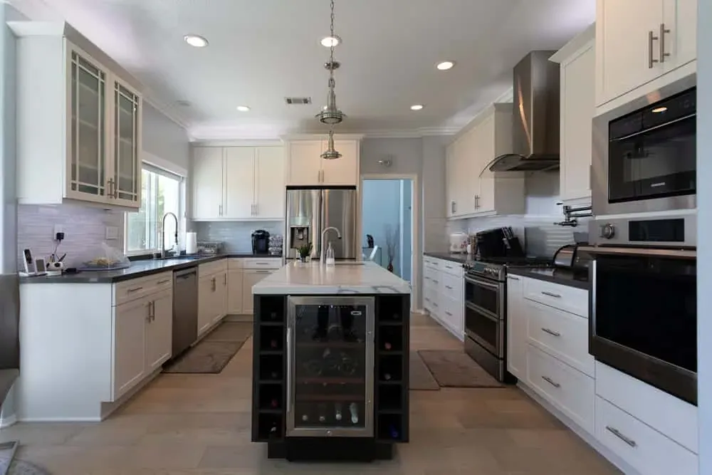 White kitchen with a dark island, wine cooler and stainless appliances