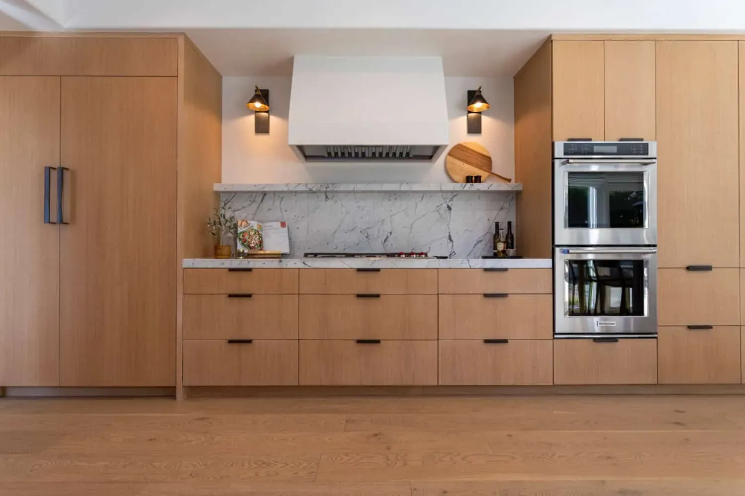 Oak cabinetry with a white plaster hood, marble backsplash and wall ovens