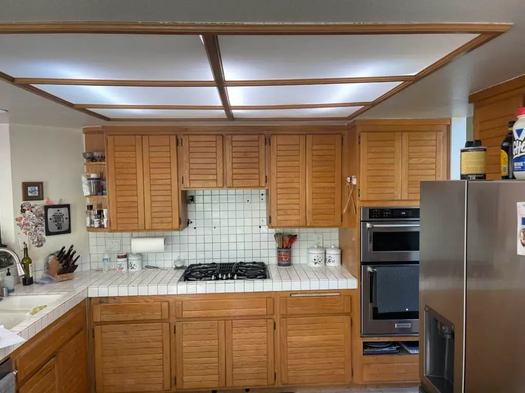 Oak kitchen before remodeling with tile counters, a cooktop and double wall ovens