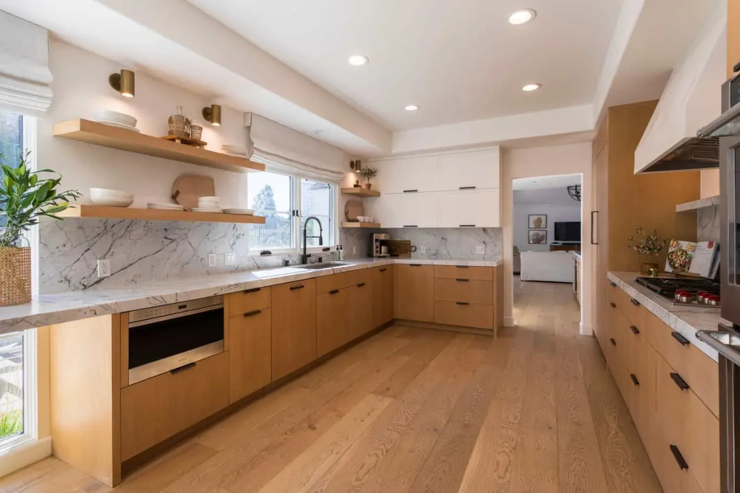 Oak kitchen with open shelving, marble counters and a window over the sink