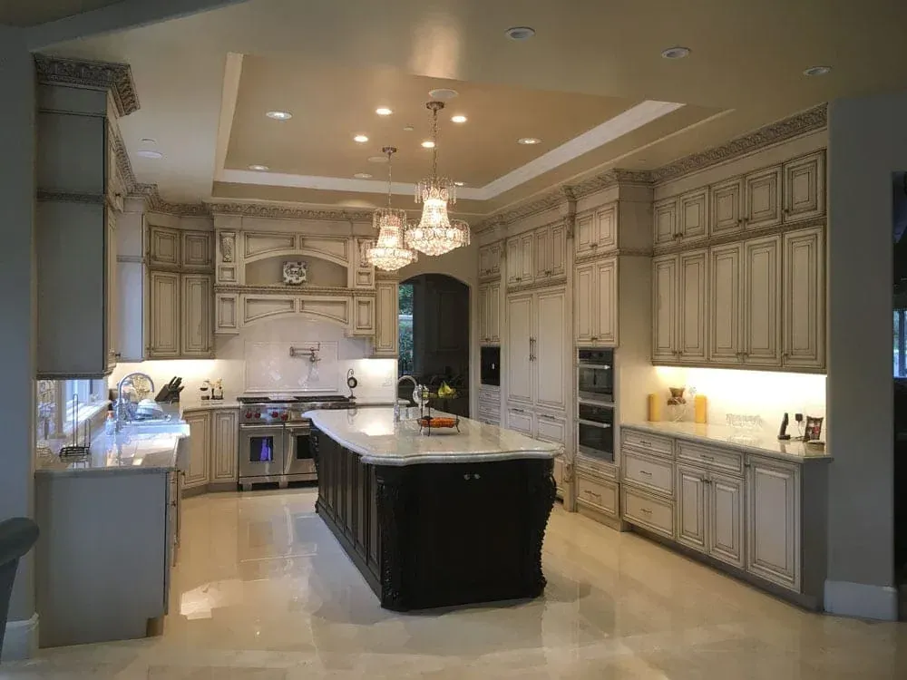Open kitchen with a tray ceiling, paired chandeliers and a dark island
