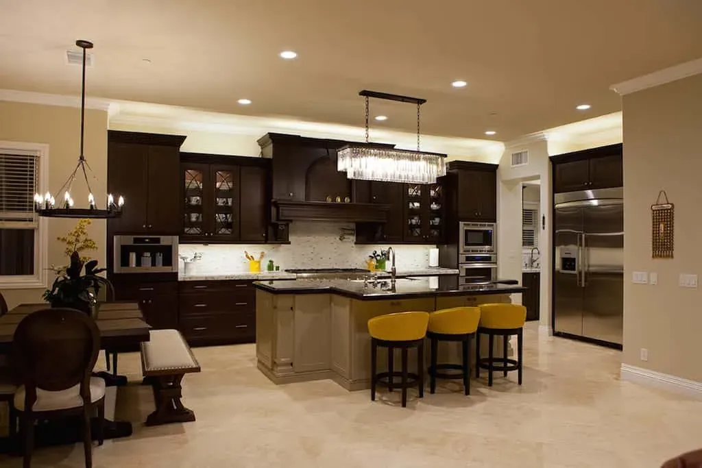 Open-plan dark kitchen with a linear chandelier and yellow bar stools