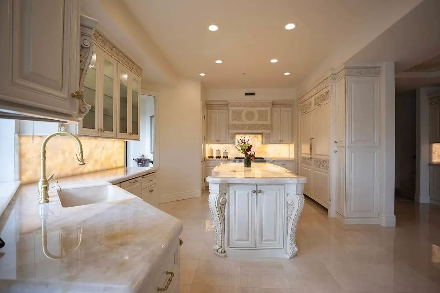 Ornate cream kitchen with a backlit onyx counter and a carved island